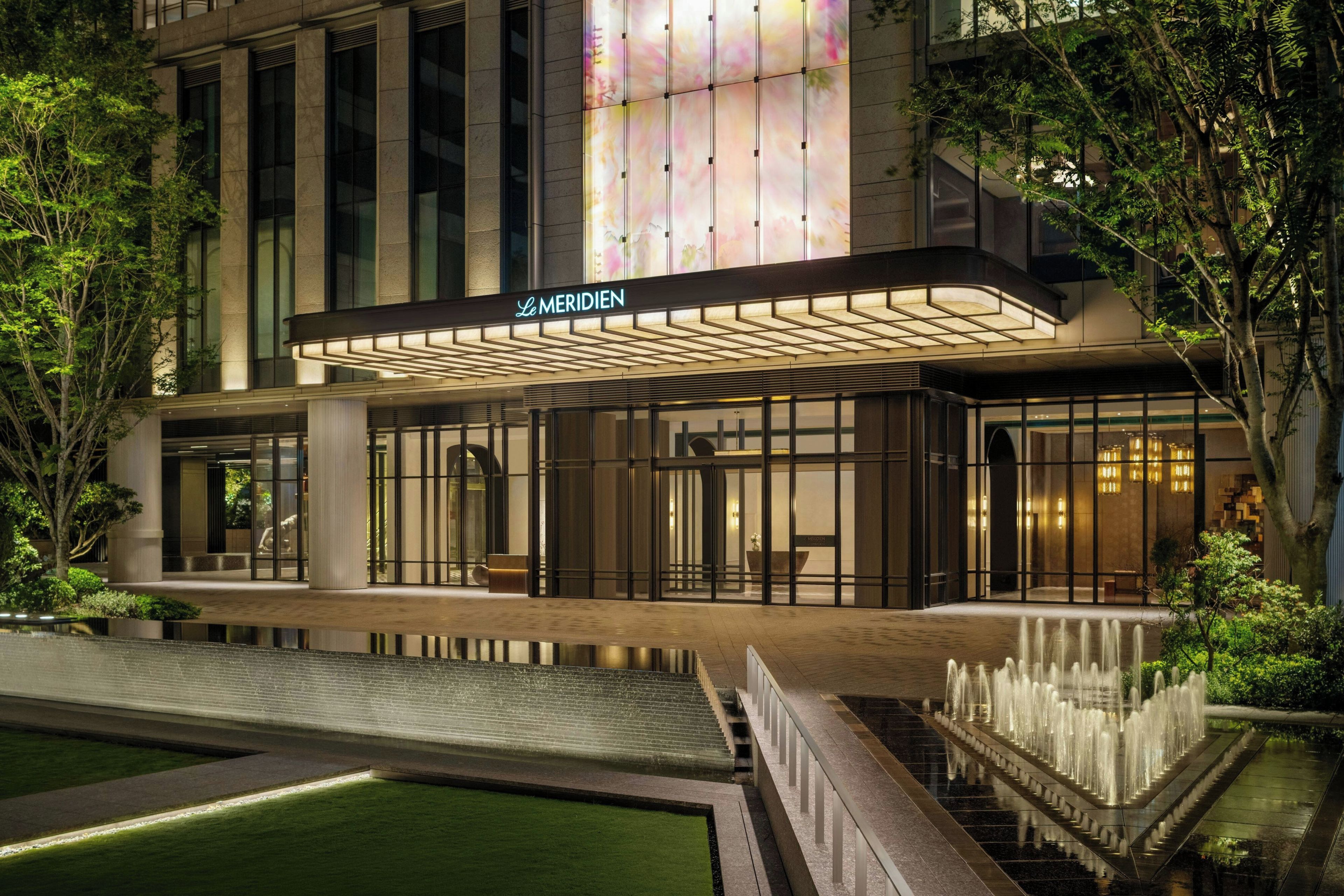 A hotel with a modern facade, a covered entrance, and a water feature in the foreground.
