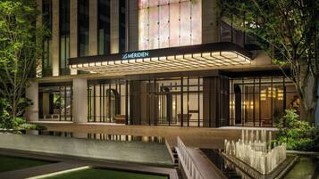 A hotel with a modern facade, a covered entrance, and a water feature in the foreground.