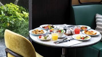 A round dining table with various dishes and drinks, surrounded by green upholstered seating.