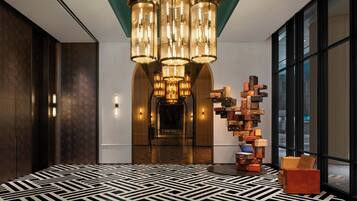 A modern lobby with a geometric patterned floor, a central chandelier, and a wall of stacked luggage.