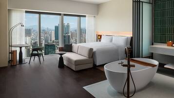Quarto de hotel moderno com uma cama grande, área de estar, escrivaninha e vista para a cidade.
