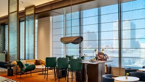 Een moderne hotellobby met een groot raam, een ronde tafel en groene stoelen.
