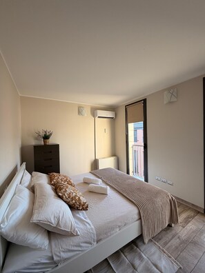 Ein modernes Schlafzimmer mit Bett, Nachttischen, einem Schminktisch und einer Klimaanlage, mit Blick nach draußen.