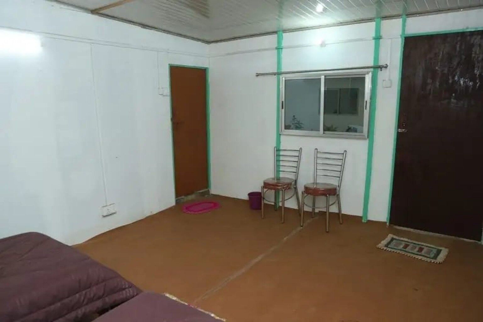 A room with a bed, two chairs, a window, and a door.