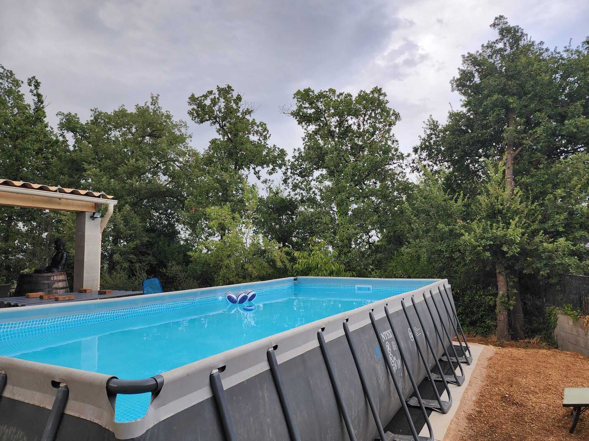 A swimming pool with a pergola and lounge chairs, surrounded by trees.