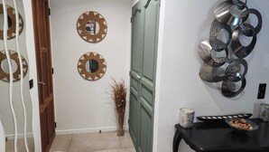 A hallway with a wooden door, two wall-mounted mirrors, a decorative metal sculpture, and a small table with a plate and a candle. - Villa 130 m², piscine au calme absolu – 8 pers. – Brignoles Var – DISPO AOÛT (Brignoles)