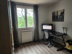 A room with a window, radiator, desk, chair, computer, and a poster on the wall. - Villa 130 m², piscine au calme absolu – 8 pers. – Brignoles Var – DISPO AOÛT (Brignoles)