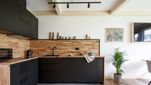 Una cocina moderna con armarios oscuros, encimera de madera y una isla grande. Hay una planta en maceta y un cuadro en la pared.