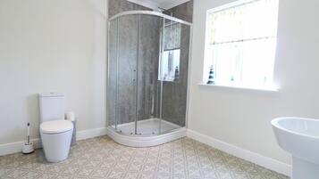 Baño con ducha de vidrio, inodoro, lavabo, baldosas de piso estampadas y ventana con cortinas.