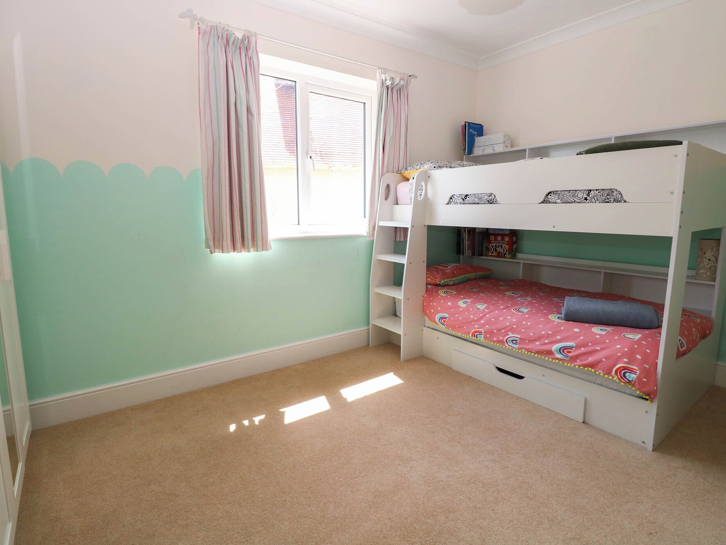 Quarto com beliche, janela, cortinas e uma estante com livros.