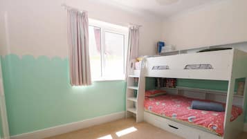 Quarto com beliche, janela, cortinas e uma estante com livros.
