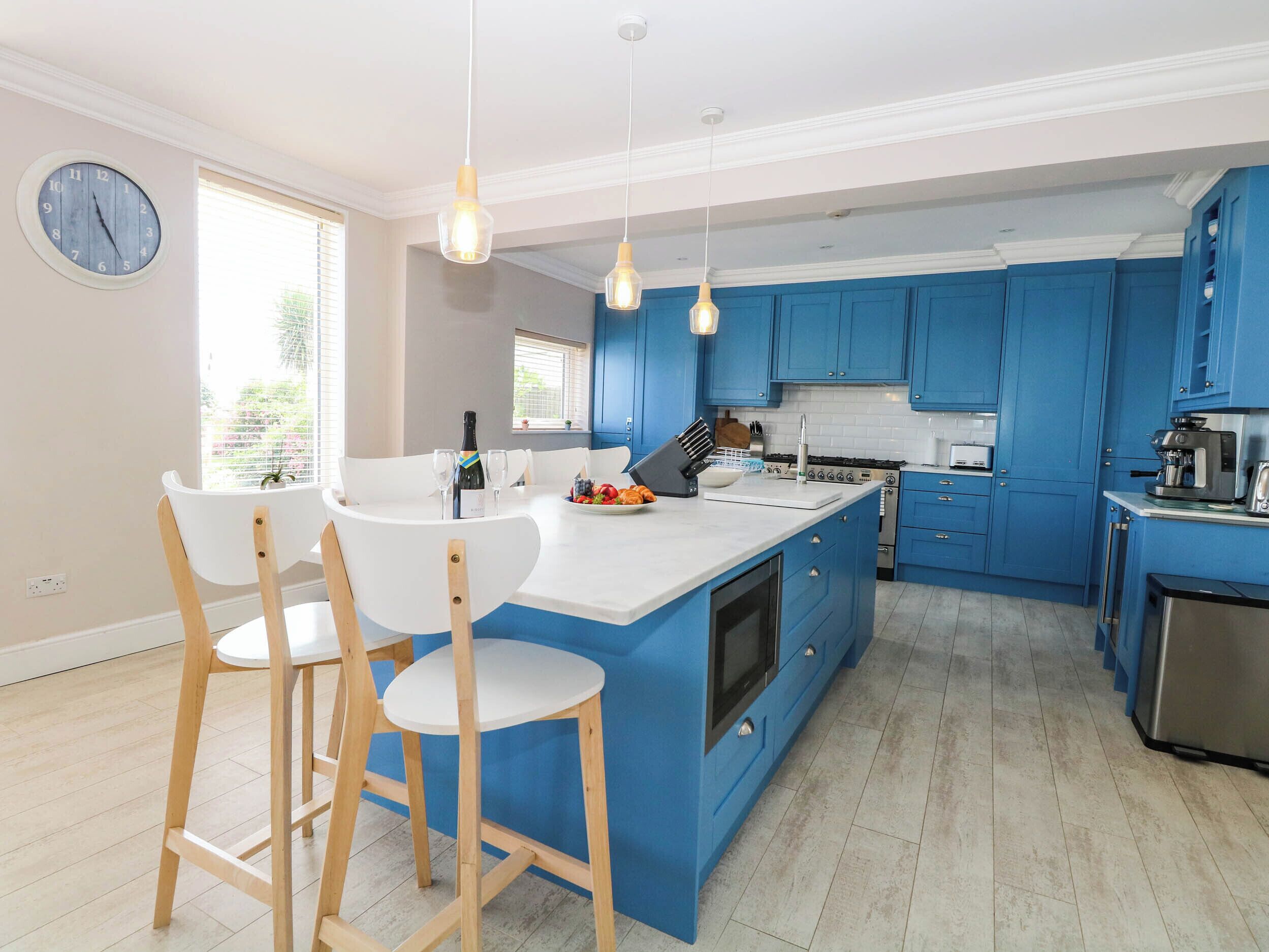 A modern kitchen with blue cabinets, a central island, and wooden bar stools.
