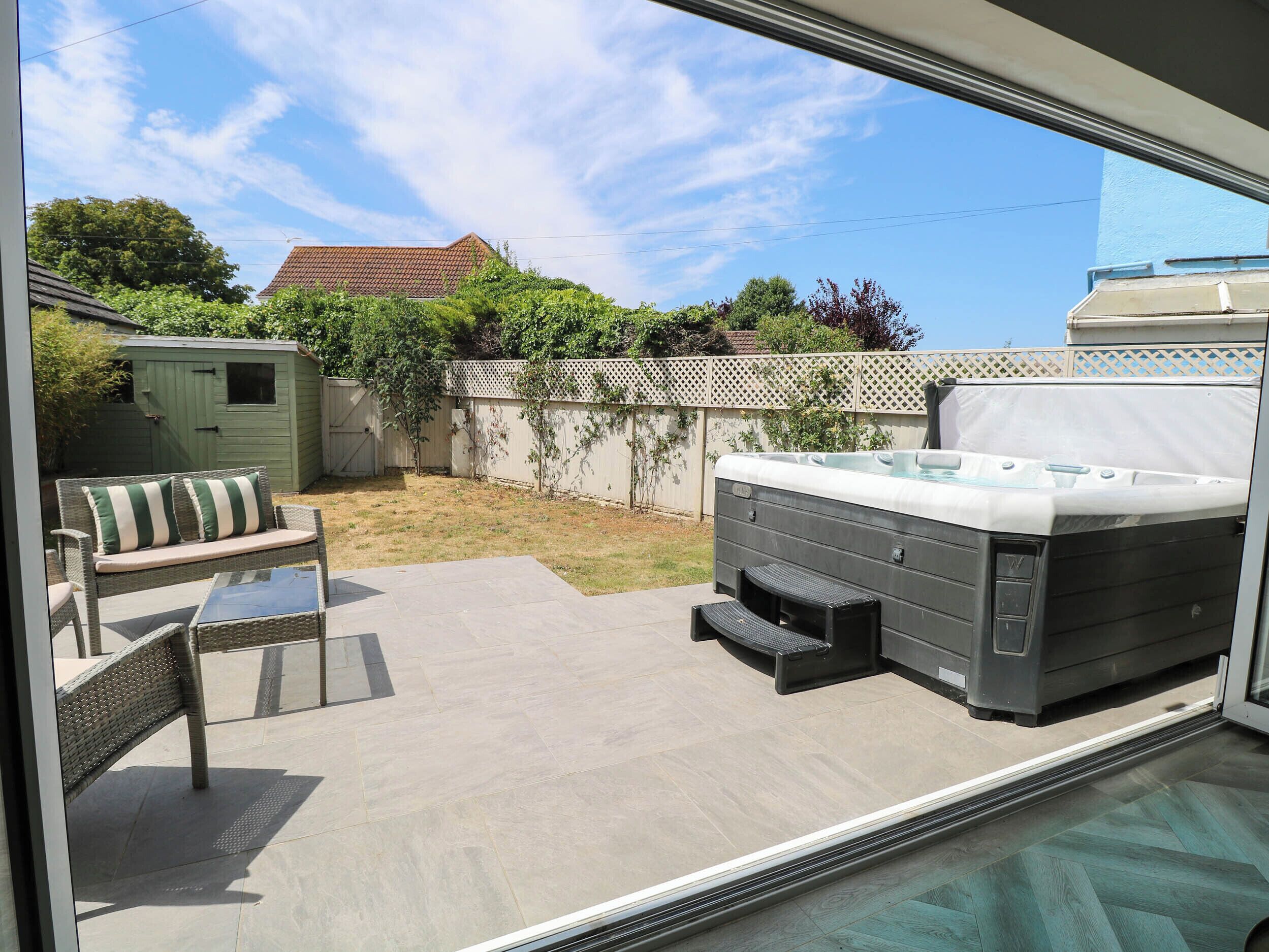 A patio with a hot tub, a covered seating area, and a fenced yard.
