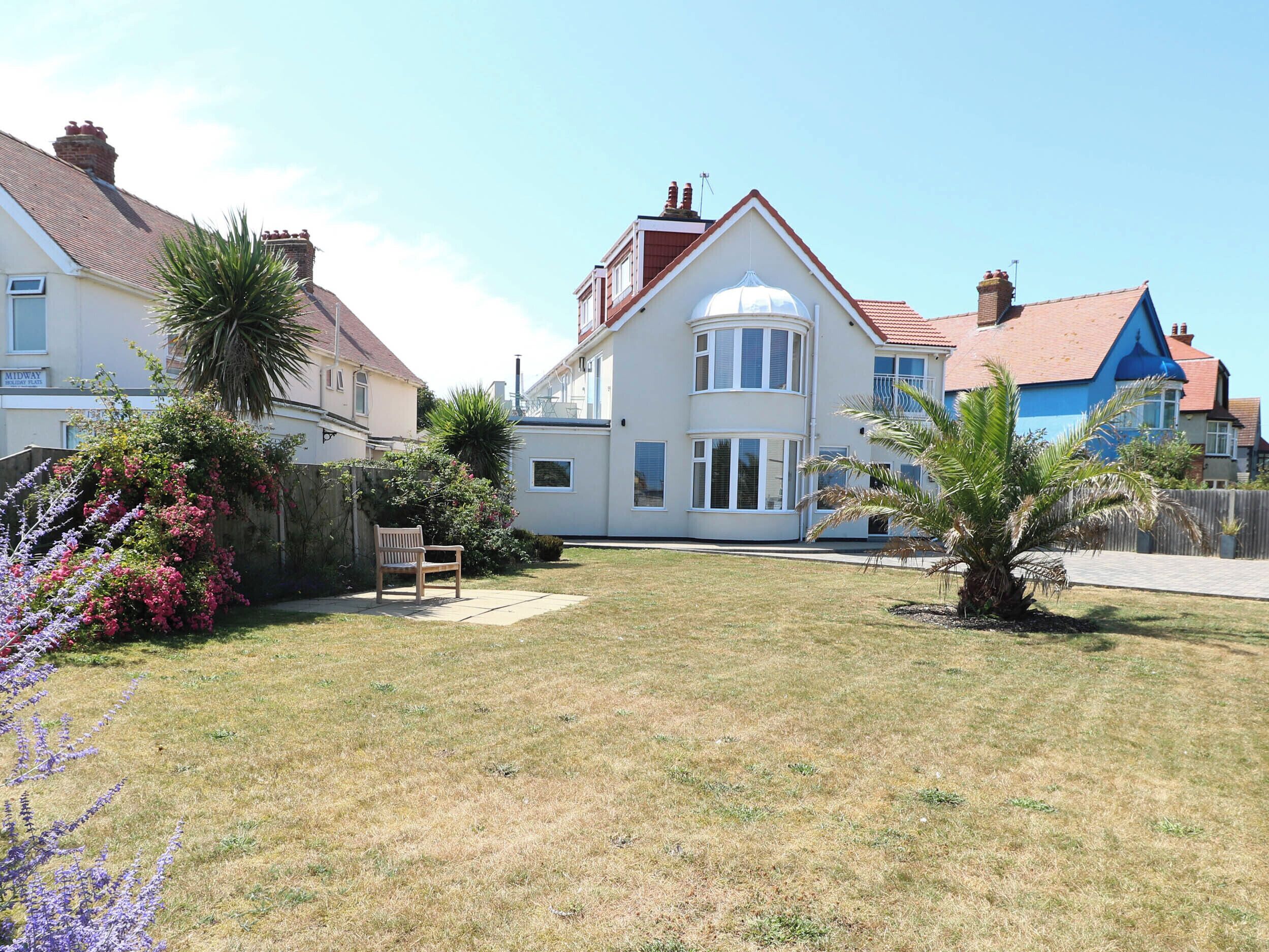 A residential property with a large lawn, a wooden bench, and a variety of plants.