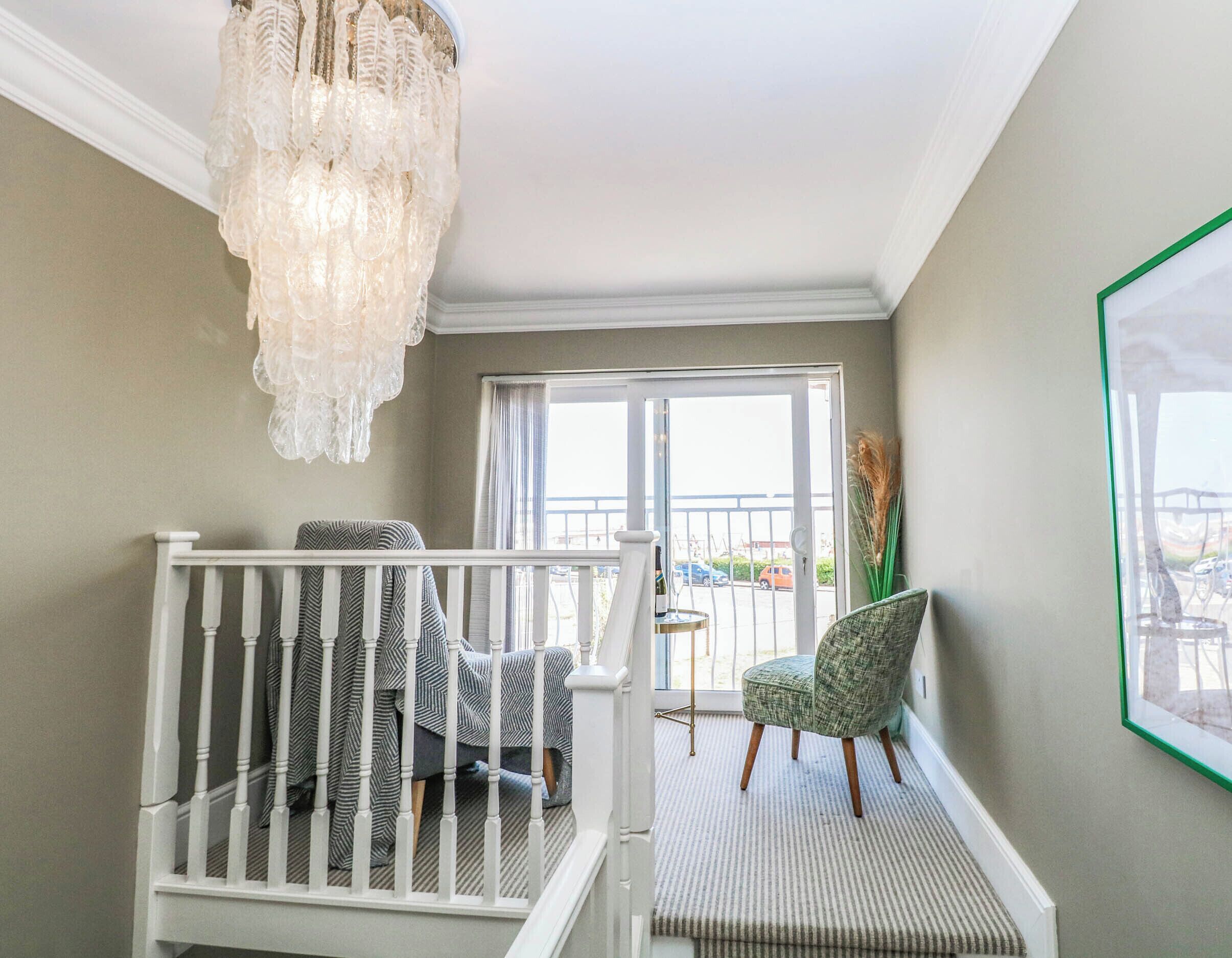 A staircase with a chandelier, a view of the outside, and a framed picture on the wall.