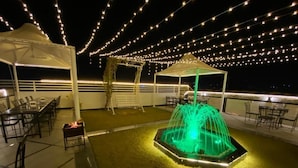Ein Außenbereich mit Tischen, Stühlen, einer Springbrunnen und Lichterketten.