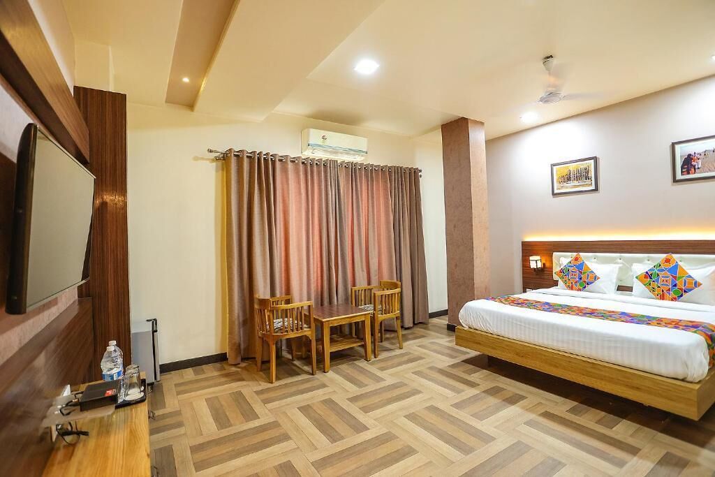 A hotel room with a bed, a desk, two chairs, a TV, and an air conditioning unit.