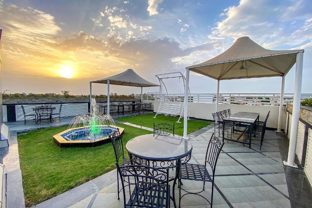 Un patio exterior con mesas y sillas, una fuente y vistas al atardecer sobre el agua.