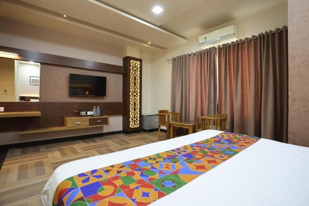 Quarto de hotel com uma cama, uma televisão, uma secretária e uma cadeira.
