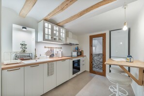 A modern kitchen with white cabinets, a wooden countertop, a built-in oven, and a stone wall.