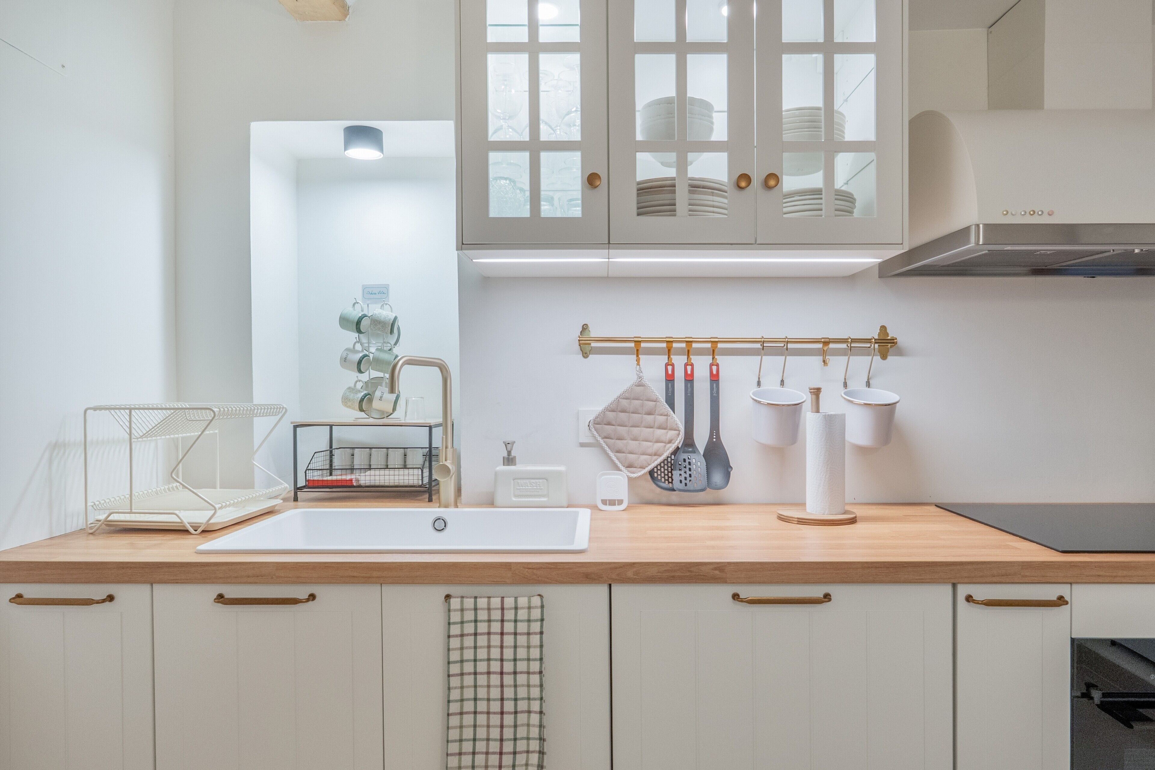 A kitchen with a white sink, a hanging spice rack, and a window above the cabinets.