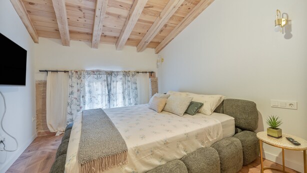 A bedroom with a wooden ceiling, a bed with a floral bedspread, a small round table with a plant, and a wall-mounted light fixture. - Holiday Home 'Ca La Mala' with Shared Terrace, Balcony and Wi-Fi (Biar)