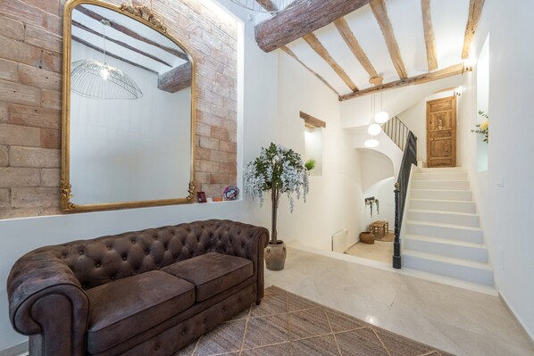 A room with a brown leather sofa, a large mirror, a potted plant, and a staircase leading to another level.