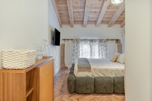A bedroom with a wooden ceiling, a bed with a floral bedspread, a small bedside table with a glass, and a knitted throw.