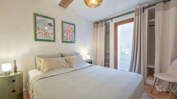 A bedroom with a bed, a nightstand, a chair, a window with curtains, and two wall art pieces.