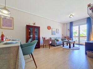 A living room with a dining area, a sofa, a cabinet, and a view through a glass door. - South-West Facing Balcony with Pool Views (Los Alcazares)