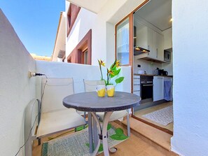 A small balcony with a table, chairs, a potted plant, and a kitchen area visible through an open door. - South-West Facing Balcony with Pool Views (Los Alcazares)