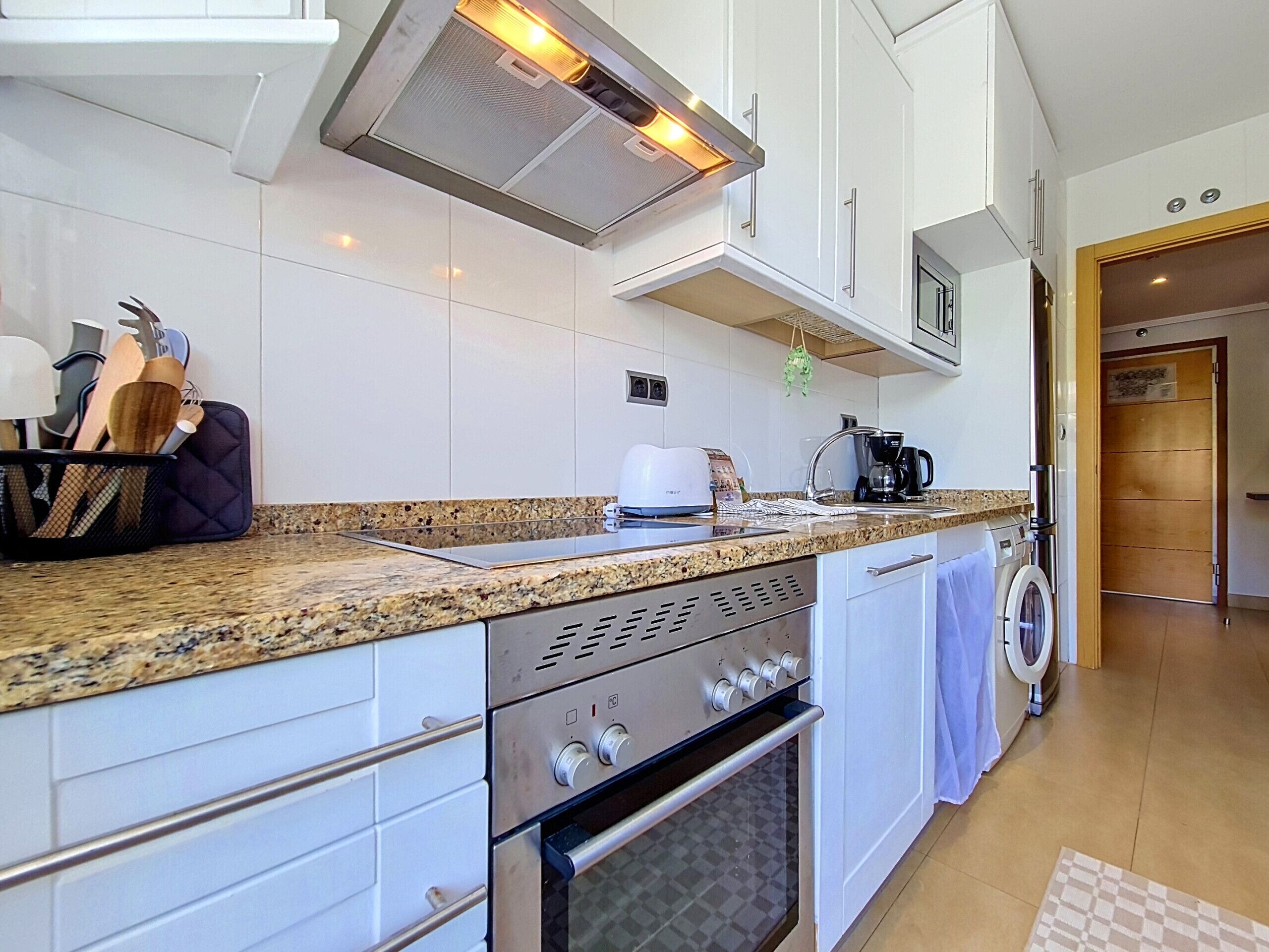 A modern kitchen with white cabinets, a granite countertop, a built-in oven, and a microwave.