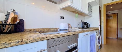 A modern kitchen with white cabinets, a granite countertop, a built-in oven, and a microwave.