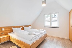 A bedroom with a wooden bed, white bedding, a nightstand, a bedside lamp, and a window with blinds. - Modern vacation home in Zirchow for a relaxing getaway in an idyllic forest setting (Zirchow)