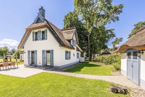 A two-story house with a thatched roof, a paved patio, and a lawn. - Modern vacation home in Zirchow for a relaxing getaway in an idyllic forest setting (Zirchow)