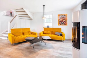 Ett modernt vardagsrum med två gula soffor, ett svart soffbord, en trappa och ett stort fönster.