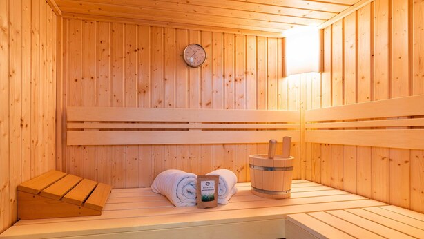A sauna with wooden benches, a sauna thermometer, and a wooden bucket.