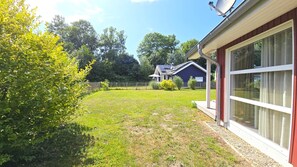 Ein Haus mit großen Glastüren, einem eingezäunten Garten und einer Solaranlage auf dem Dach.