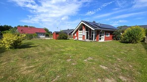 A red house with a sloped roof and solar panels, surrounded by a grassy yard and a wooden fence. - Kiek Ut Vacation Home – Baltic Sea, Sauna, and Vacations with Your Dog (Schönberg (Holstein))