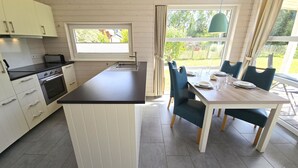 Et moderne køkken med en central ø, et spiseområde med bord og stole, samt et vindue med gardiner.