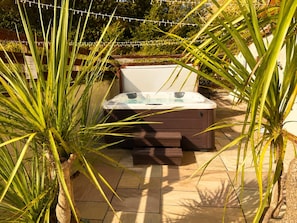 A hot tub in an outdoor setting with a wooden deck and potted plants. - Finest Retreats - Bryncoch Retreat (Bryncoch)