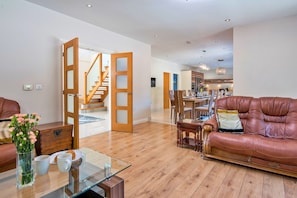 A spacious living room with a leather sofa, a glass coffee table, and a dining area with wooden chairs. - Finest Retreats - Bryncoch Retreat (Bryncoch)