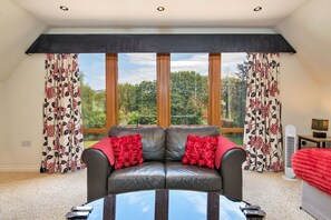 A room with a large window, a leather sofa with red cushions, a small table, and a fan.