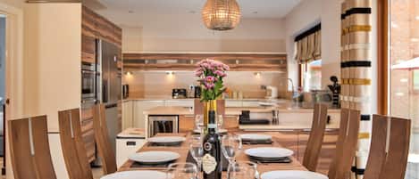 A dining area with a wooden table set for six, a vase of flowers, and a bottle of wine.