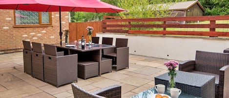 An outdoor patio with wicker furniture, a red umbrella, and a table set for dining.