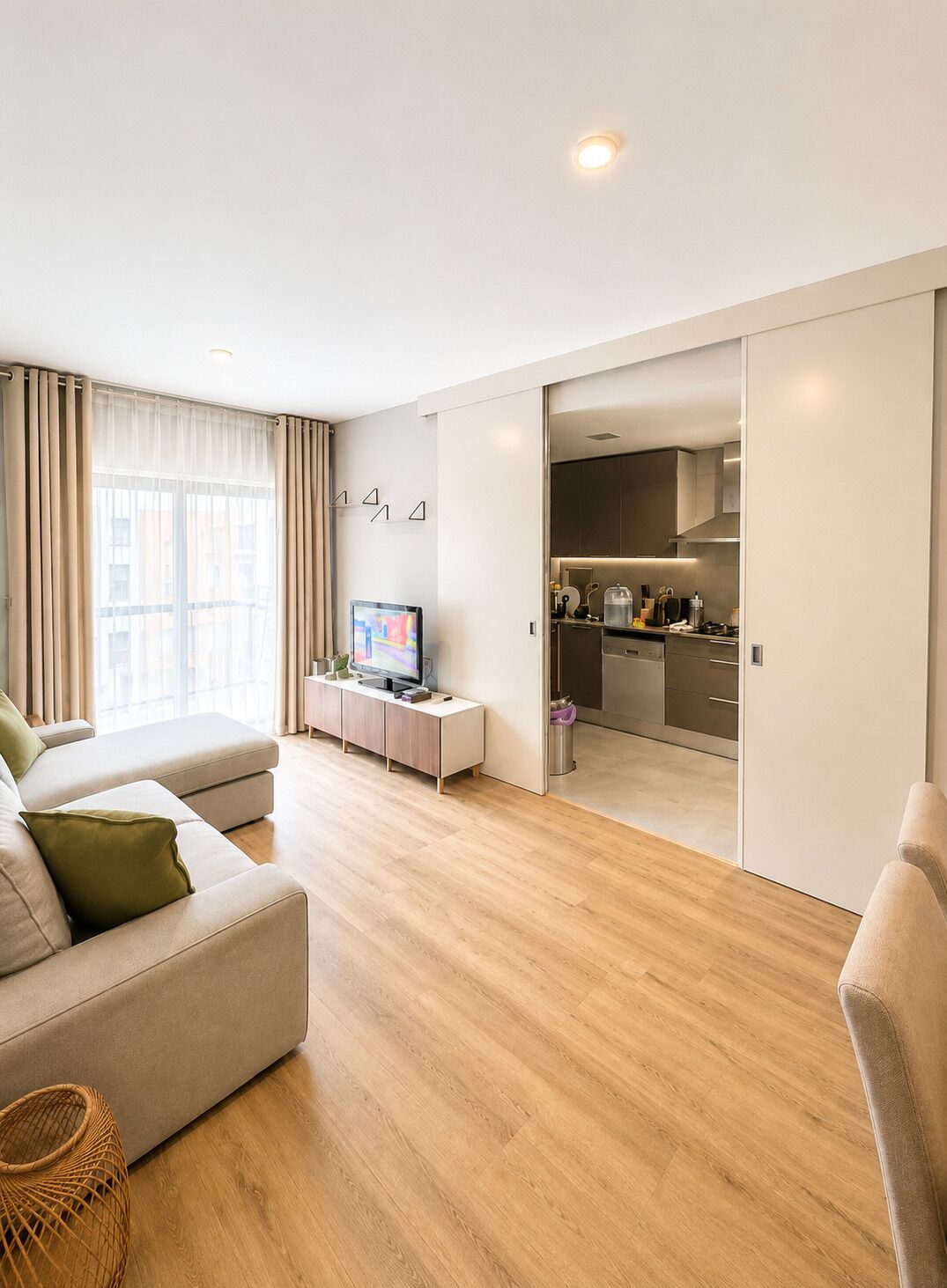 Una sala moderna con un sofá, un televisor y una cocina a la vista a través de una puerta abierta.