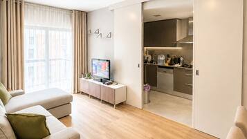 Una sala moderna con un sofá, un televisor y una cocina a la vista a través de una puerta abierta.