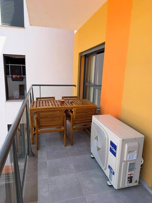 A balcony with a wooden table and chairs, a window with a view, and a white Haier air conditioner.