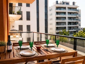 A balcony with a wooden table set for dining, a bottle of wine, and green glassware.