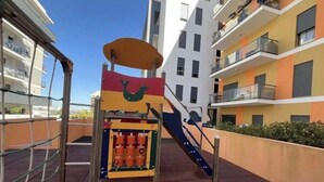 En lekplats med en rutschkana och klätterställningar, omgiven av flerfamiljshus.